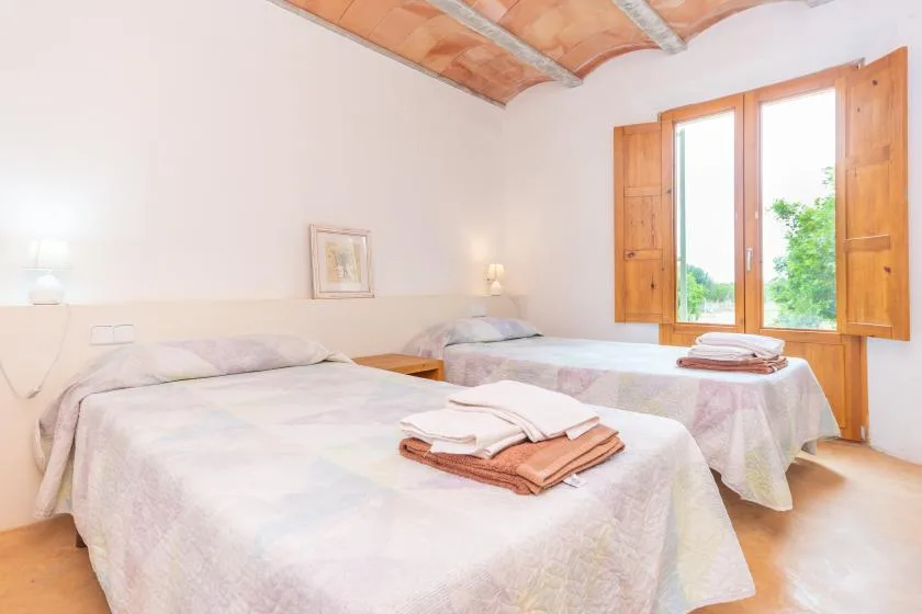 A bright bedroom with two beds and an open window overlooking greenery.
