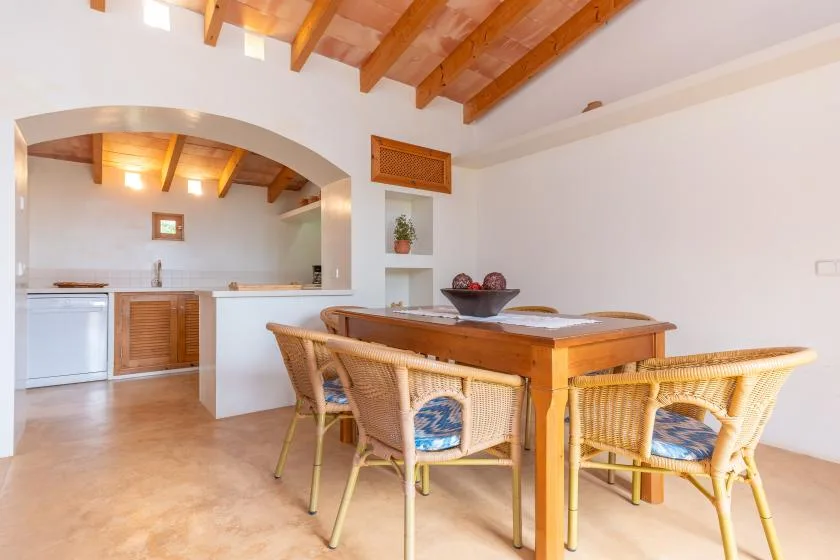 A dining area with a wooden table and woven seating beside an open kitchen.