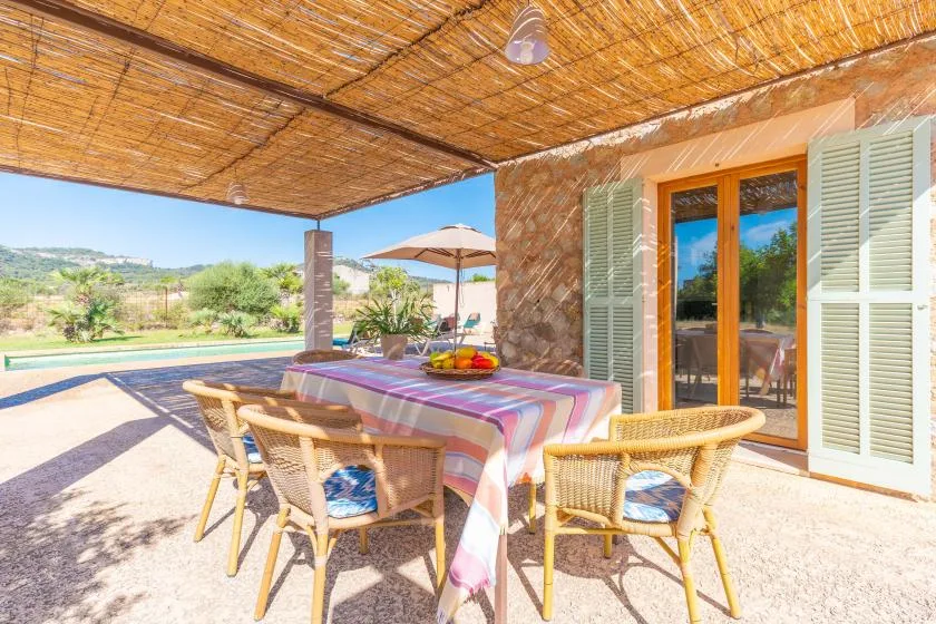 A shaded outdoor dining area with a table overlooking a swimming pool and countryside.