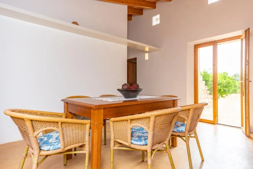 A dining area with a wooden table and woven seating beside an open glass door.