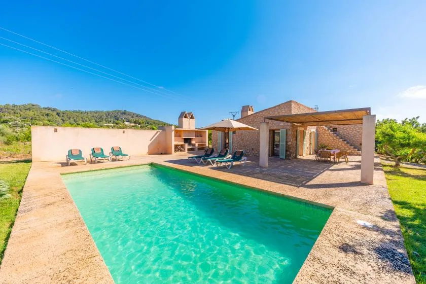 Outdoor swimming pool beside a stone house and shaded patio.