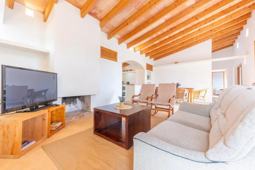 A bright living room with seating, a television, and an exposed wooden ceiling.