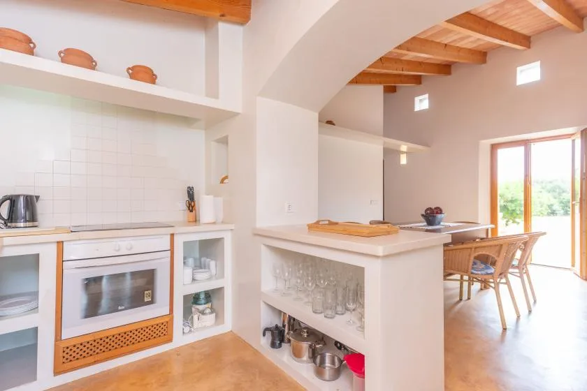 A bright kitchen opens onto a dining area, with wooden beams overhead.