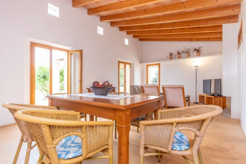 A dining area with a large wooden table and wicker seating beneath exposed beams.