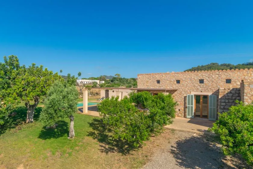 A stone building beside a garden with trees and a small pool.