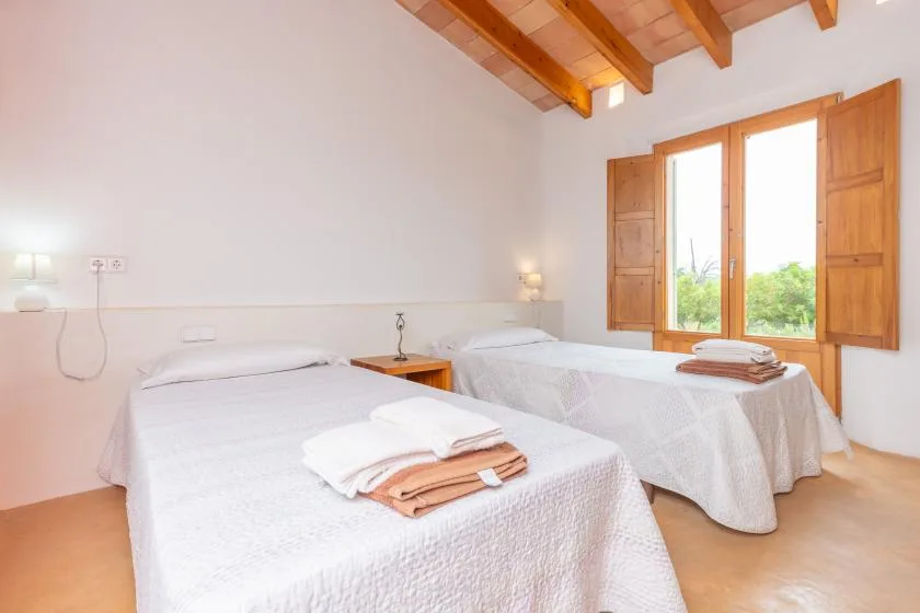 A bright bedroom with two beds and wooden shutters open to a window.