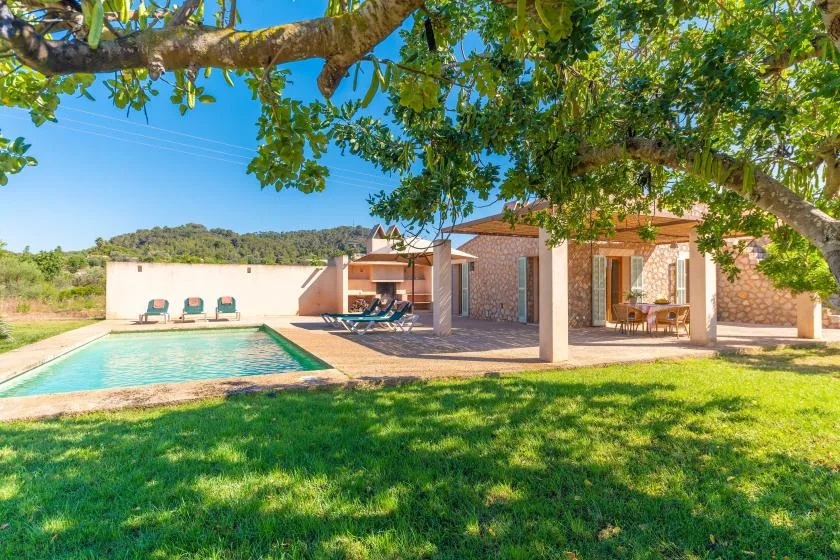 A house and patio overlook a swimming pool and lawn beneath leafy trees.