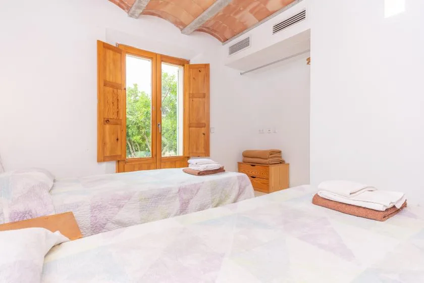 A bedroom with two beds and an open wooden window.
