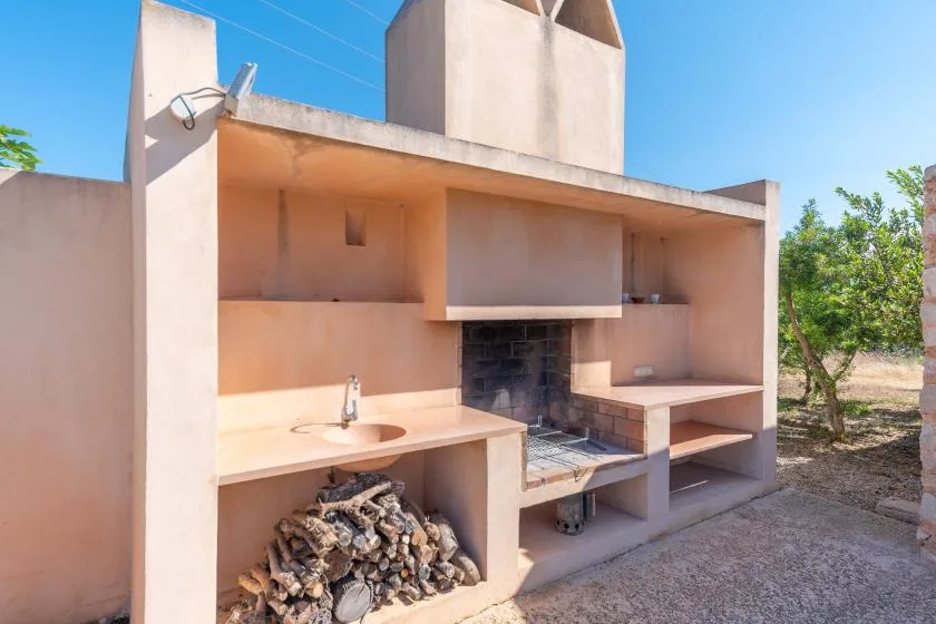 An outdoor masonry cooking area with a built-in grill and stacked firewood.
