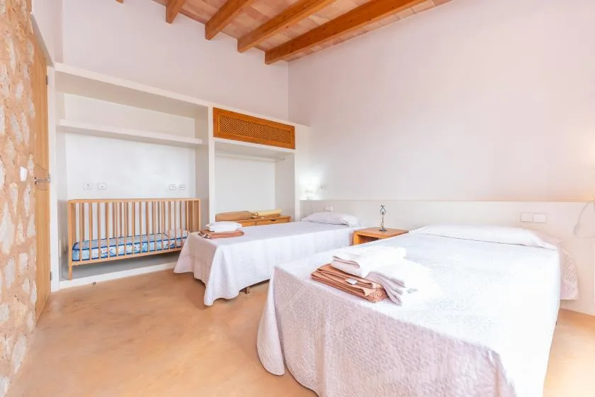 A bright bedroom with beds, white linens, and exposed wooden ceiling beams.