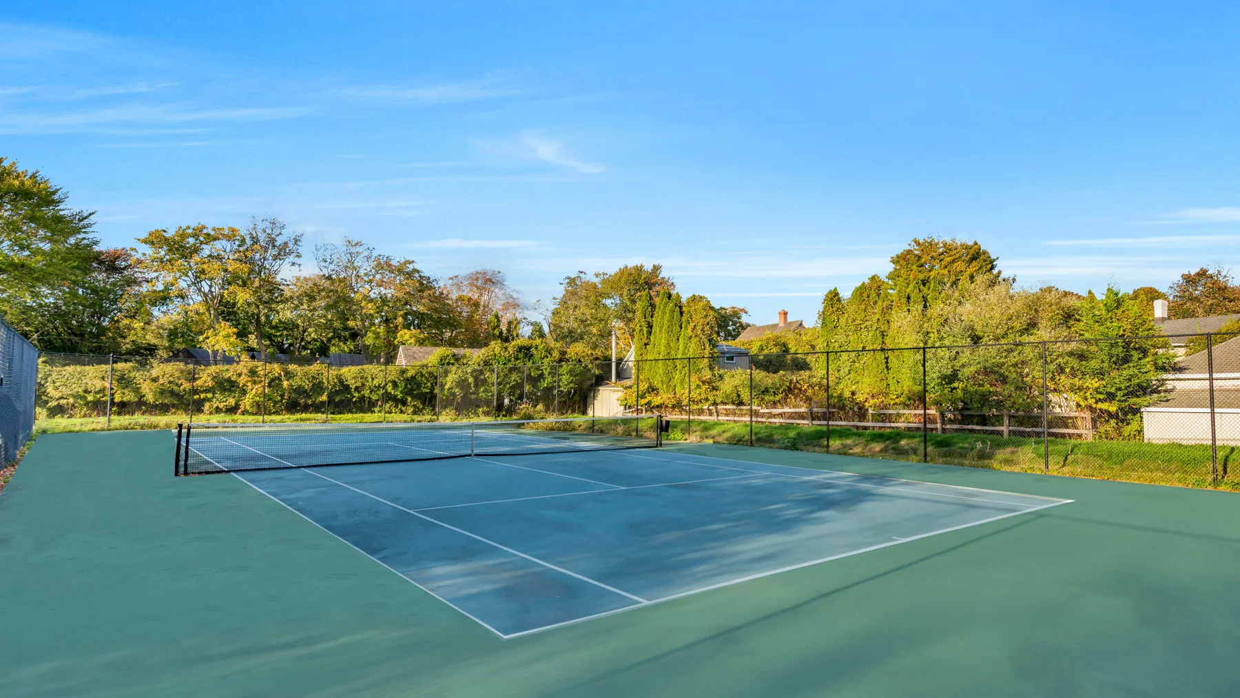 Una cancha de tenis al aire libre está rodeada de cercas y árboles.