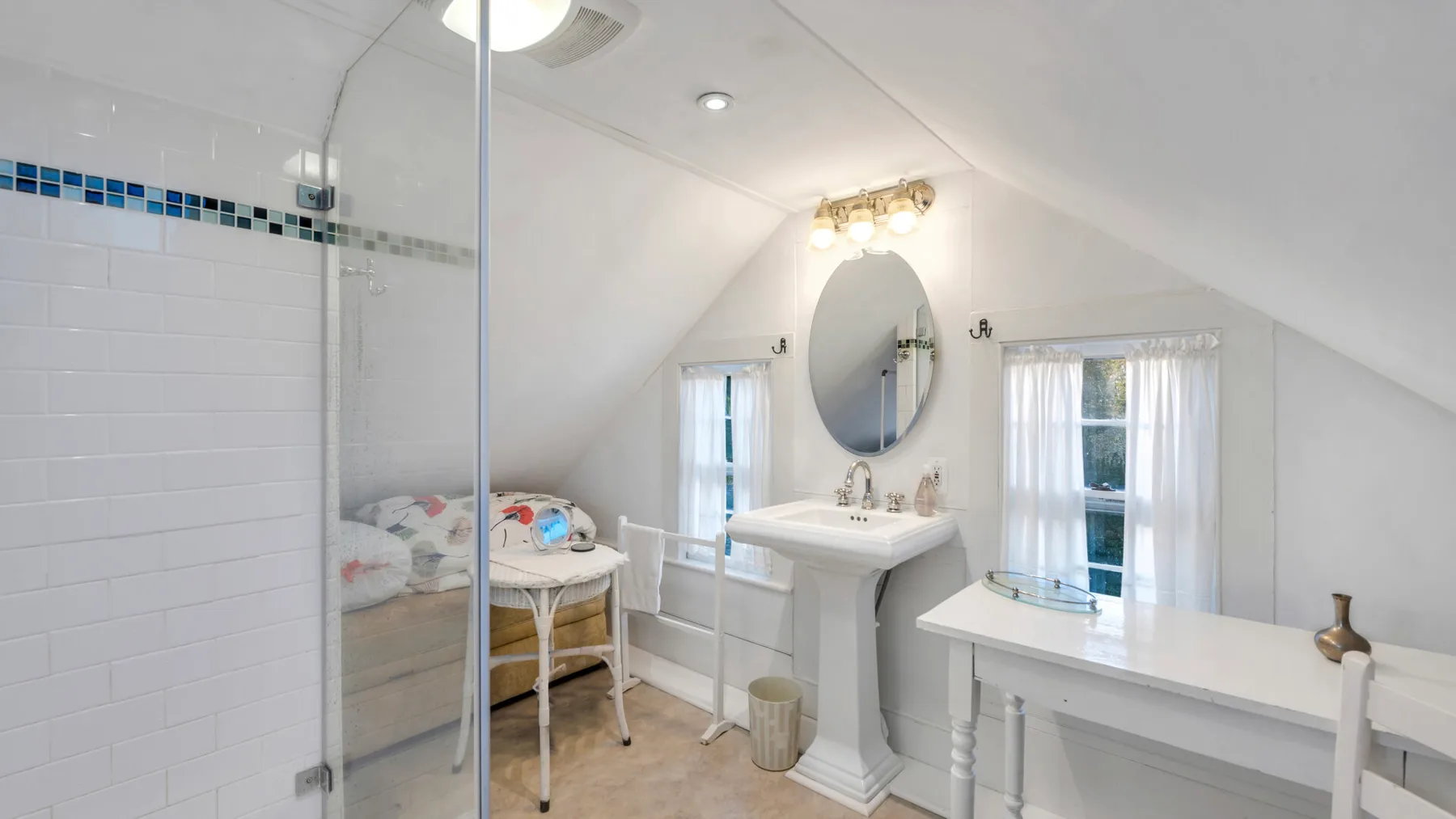 Un baño luminoso con ducha de vidrio, lavabo de pedestal y tocador.