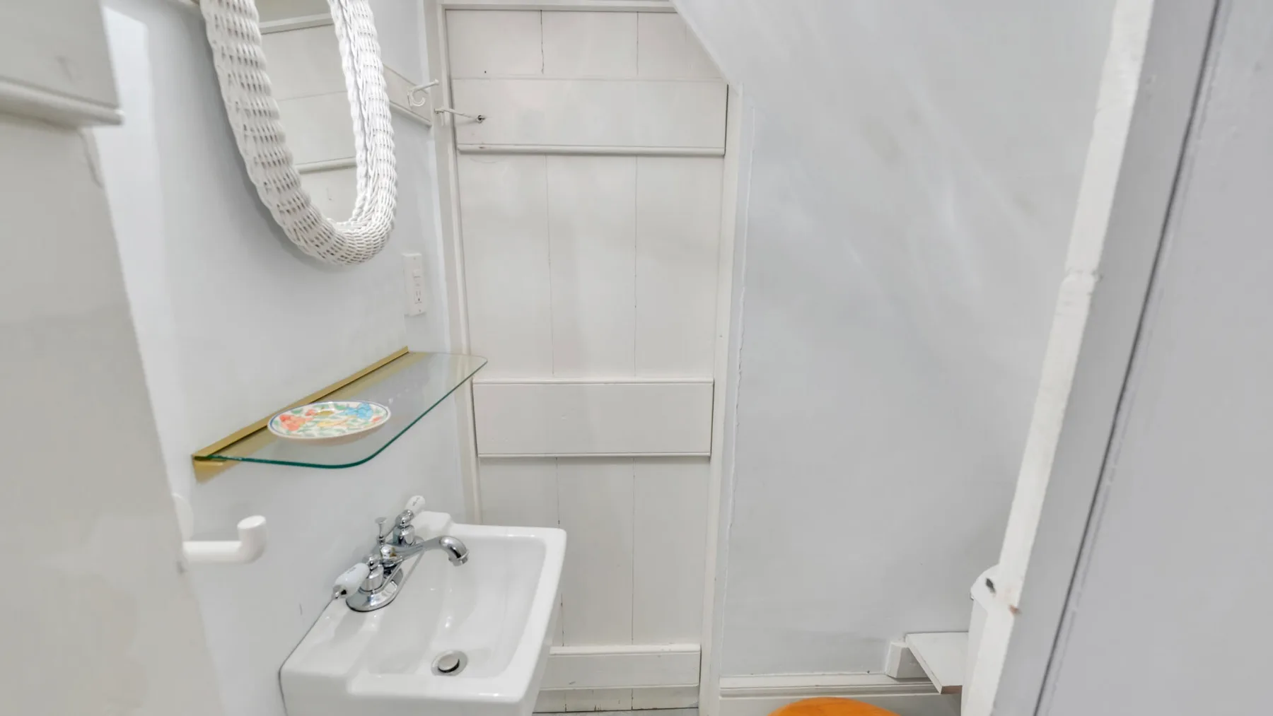 Un baño compacto con un lavabo de pared y una repisa de vidrio.