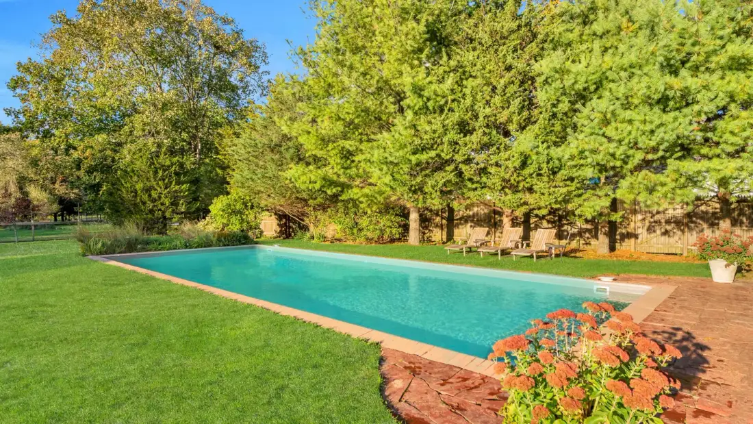 Una piscina al aire libre está junto a un césped y árboles frondosos.