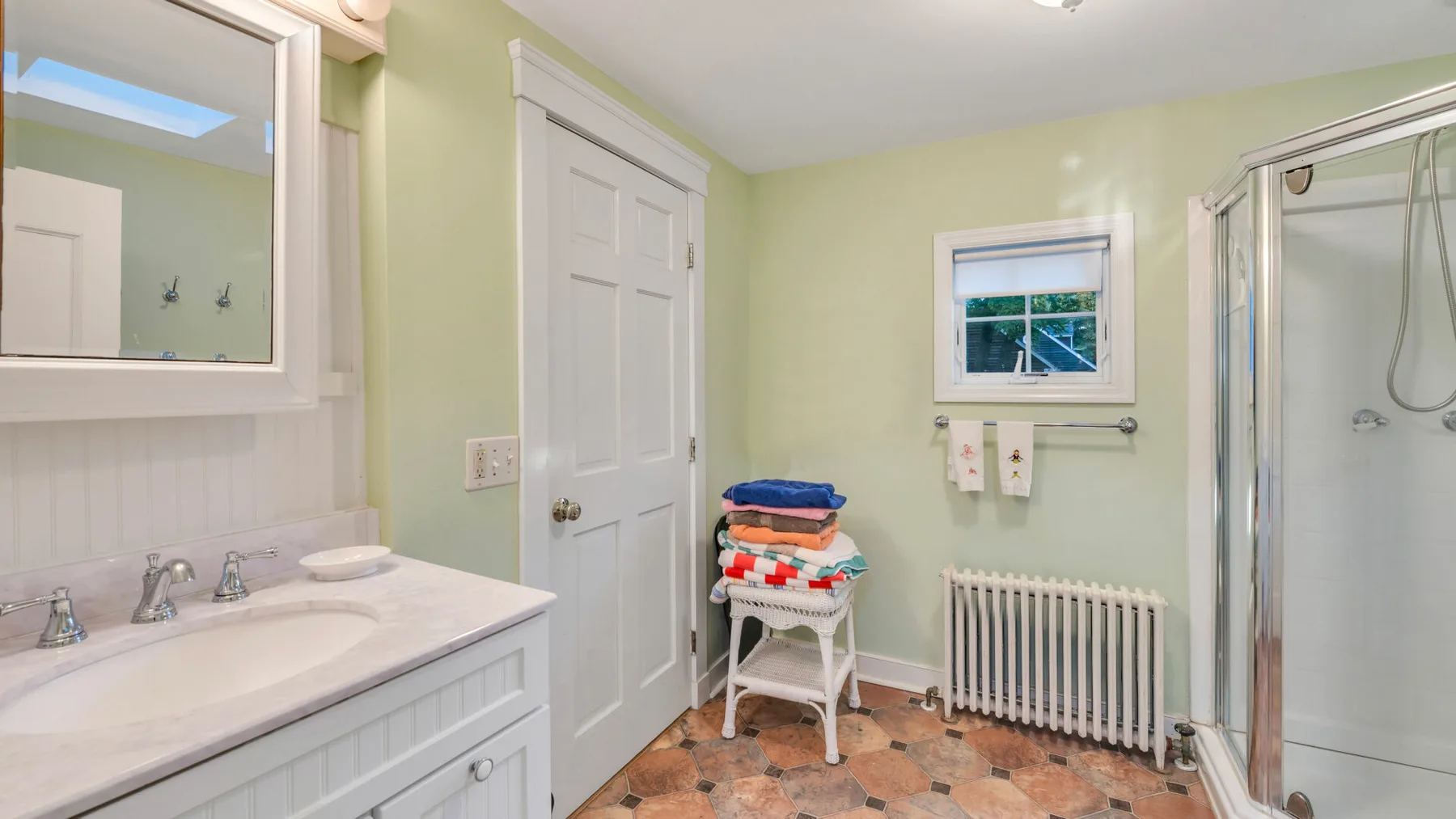 Un baño con lavabo, ducha y radiador debajo de una ventana pequeña.