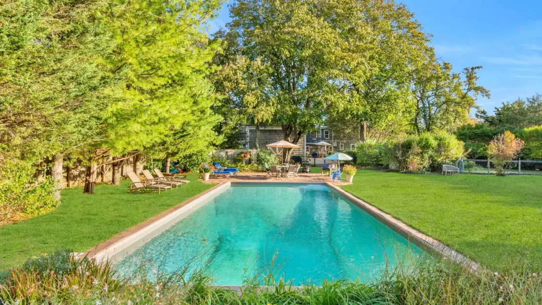 Una piscina en el patio está rodeada de césped verde y árboles.