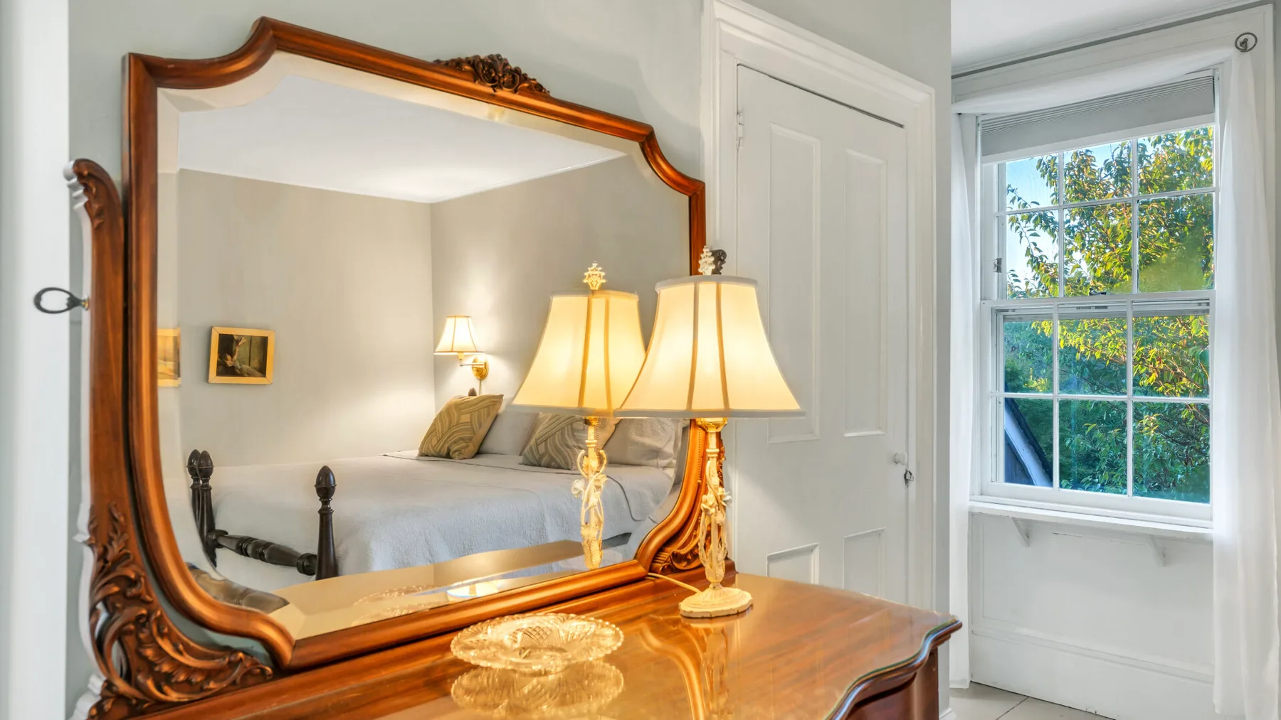Un dormitorio con un espejo grande y ornamentado, lámparas y una ventana.
