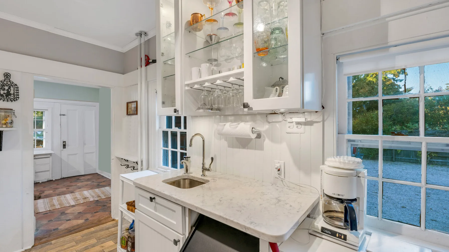 Una cocina luminosa con encimera, fregadero, gabinetes de vidrio y una ventana.
