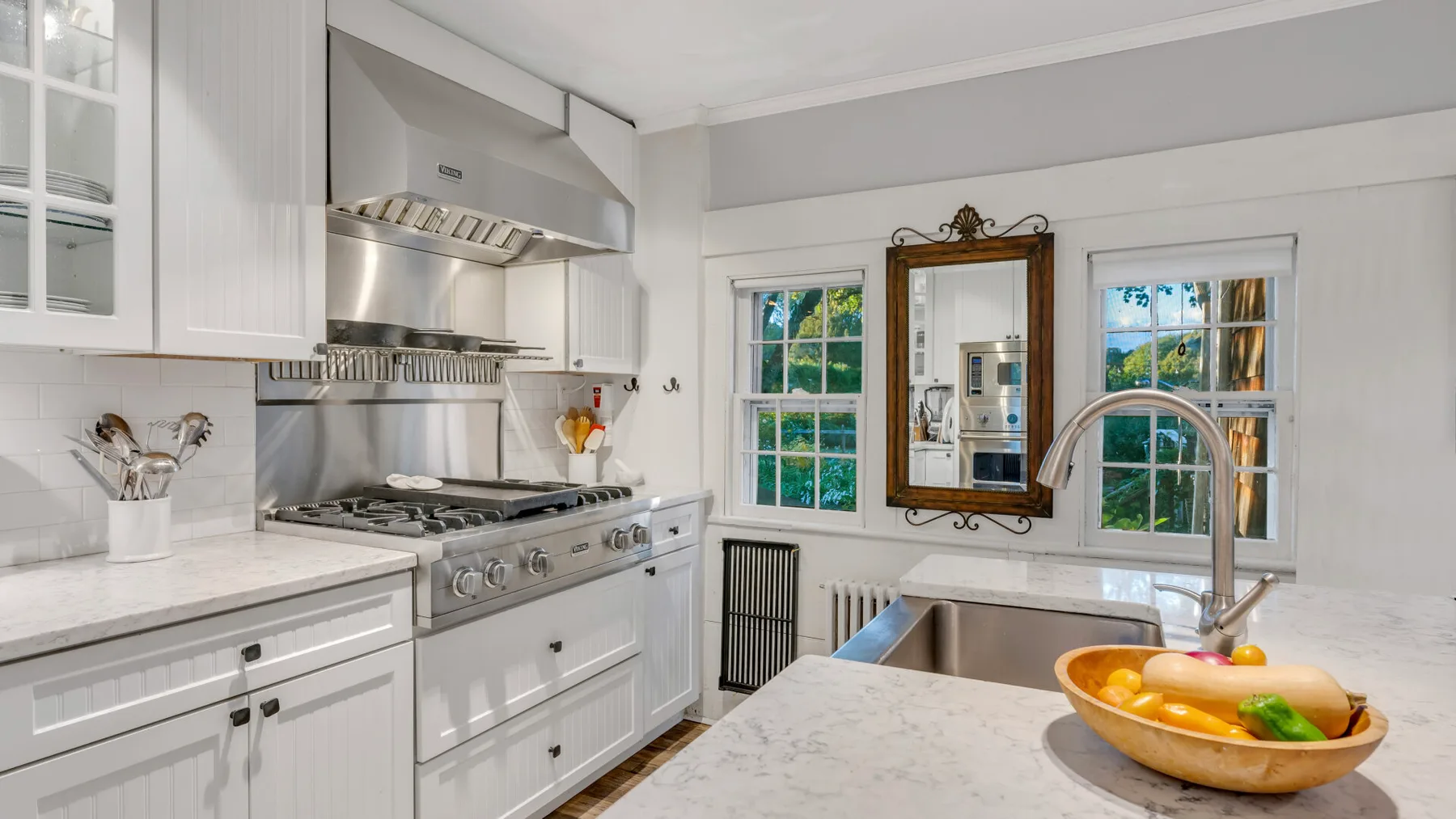 Una cocina blanca y luminosa con una estufa grande y un fregadero en la isla central.