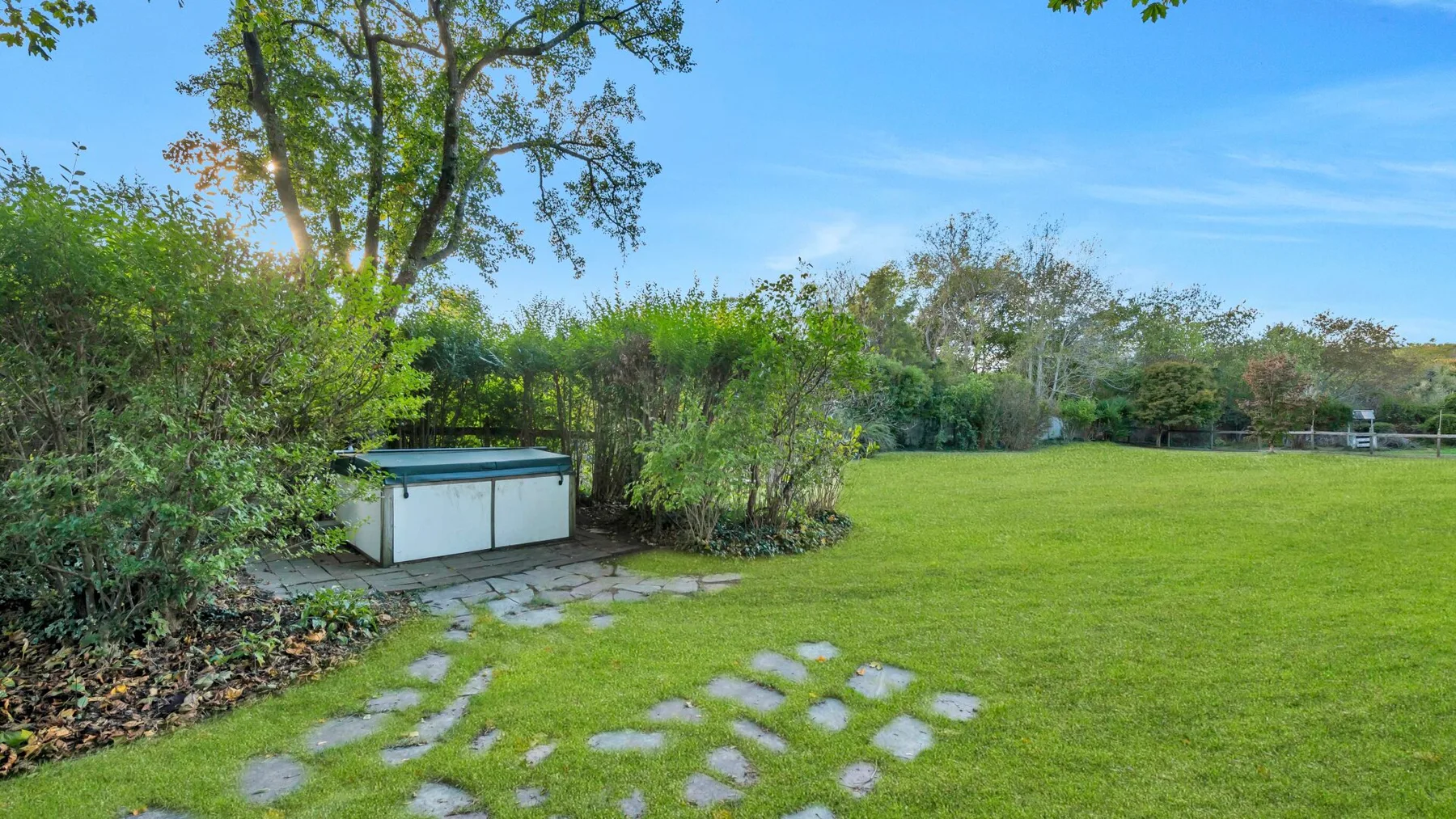 Un jardín con césped, piedras de paso y una pequeña construcción blanca.