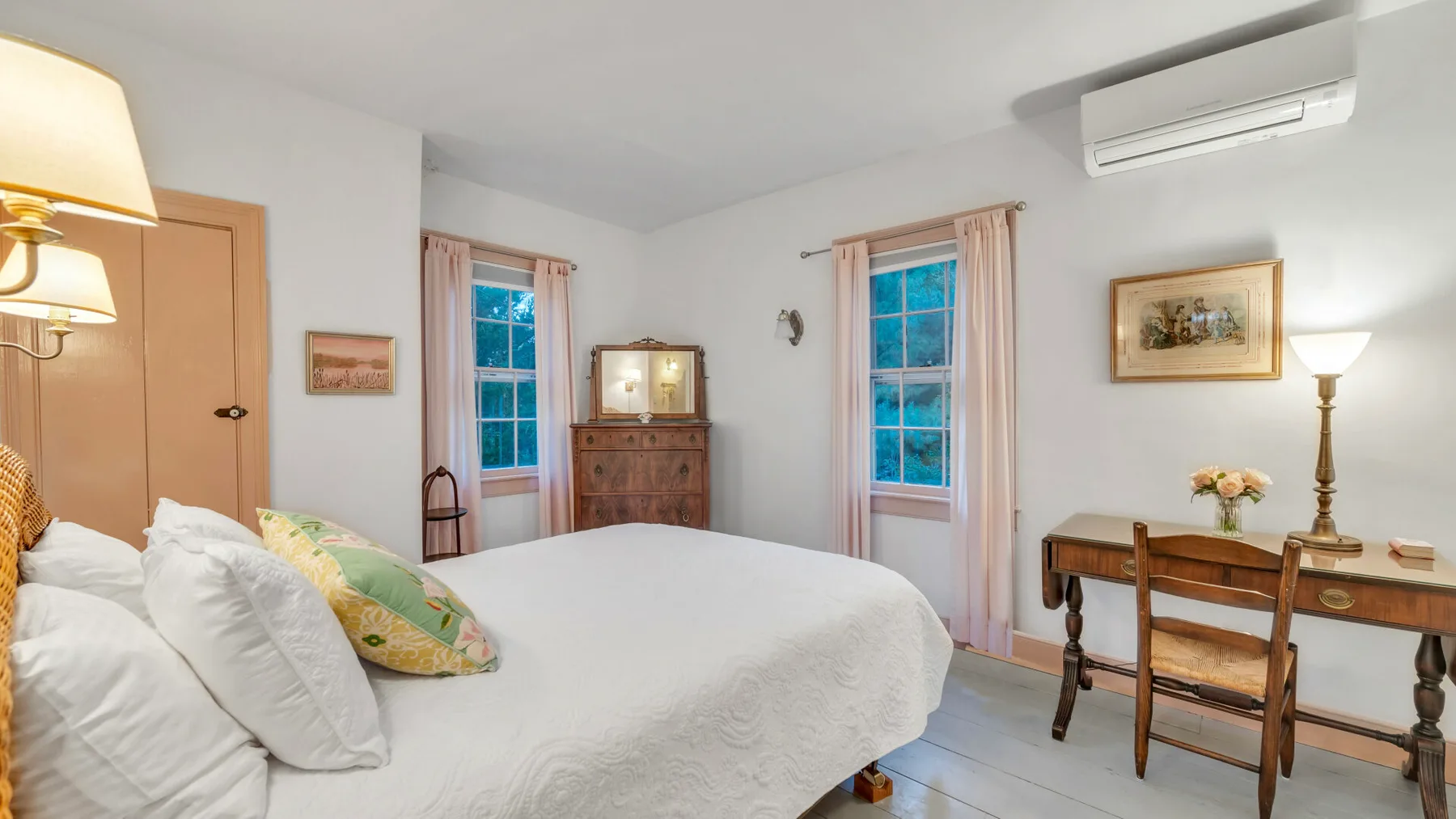 Un dormitorio con una cama, una cómoda de madera y un escritorio junto a las ventanas.