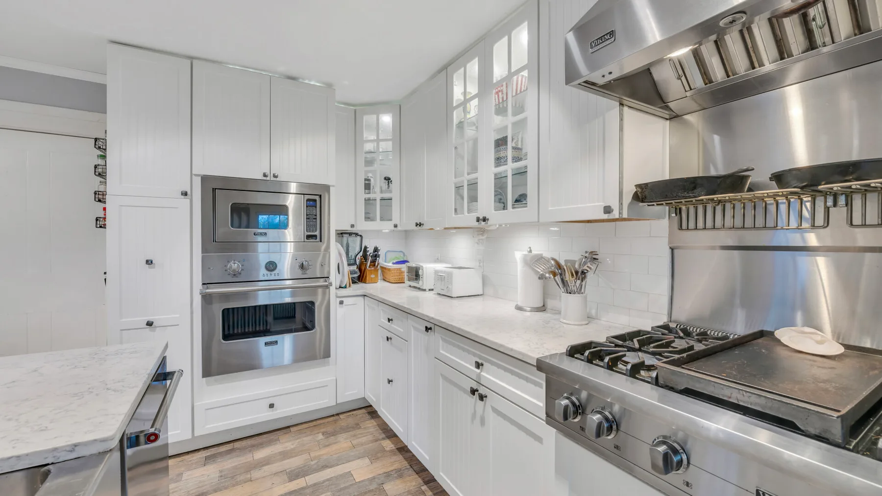 Una cocina luminosa con gabinetes blancos, un horno empotrado y una estufa de acero inoxidable.