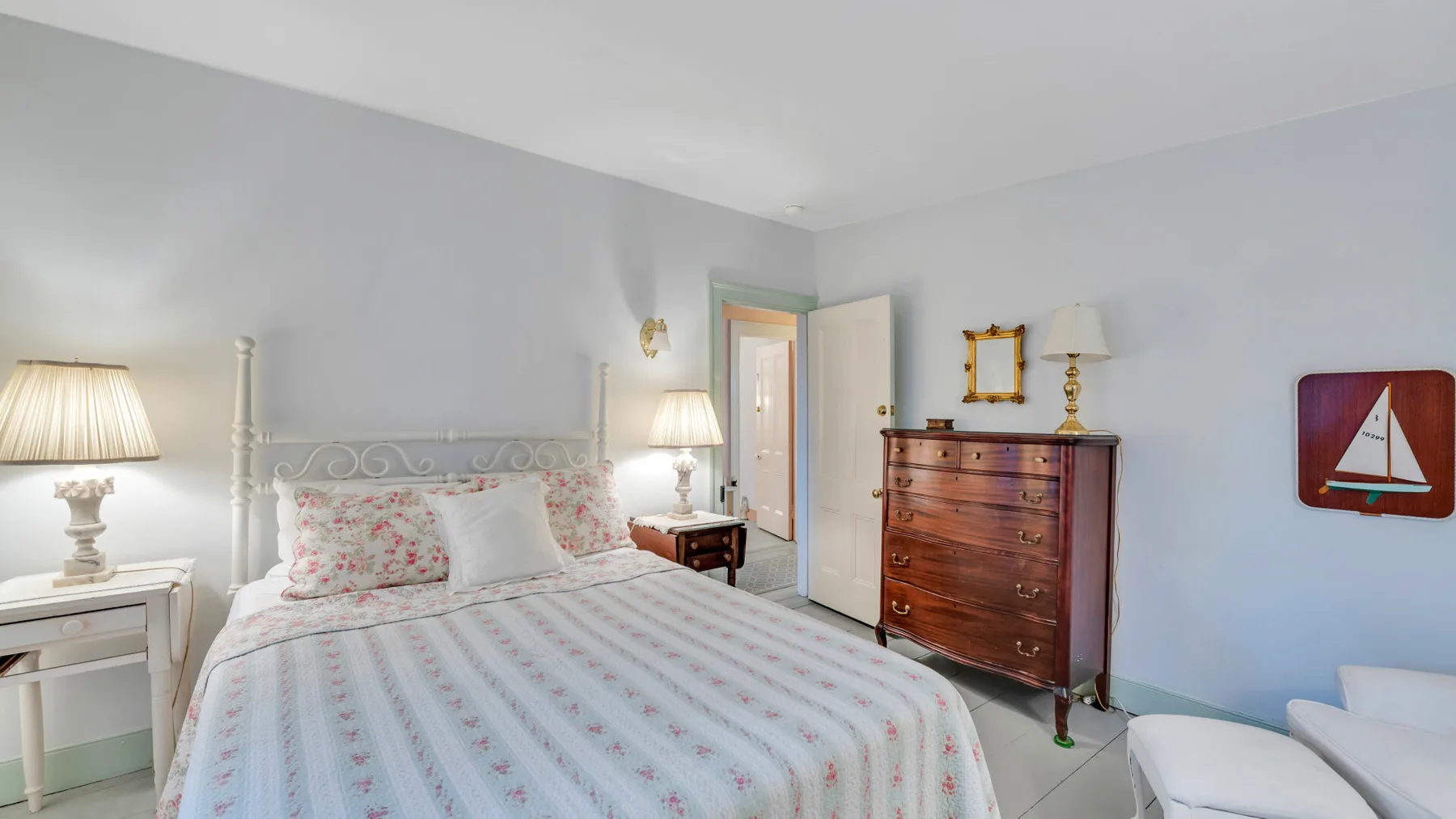 Un dormitorio con una colcha floral, mesitas de noche y una cómoda de madera.