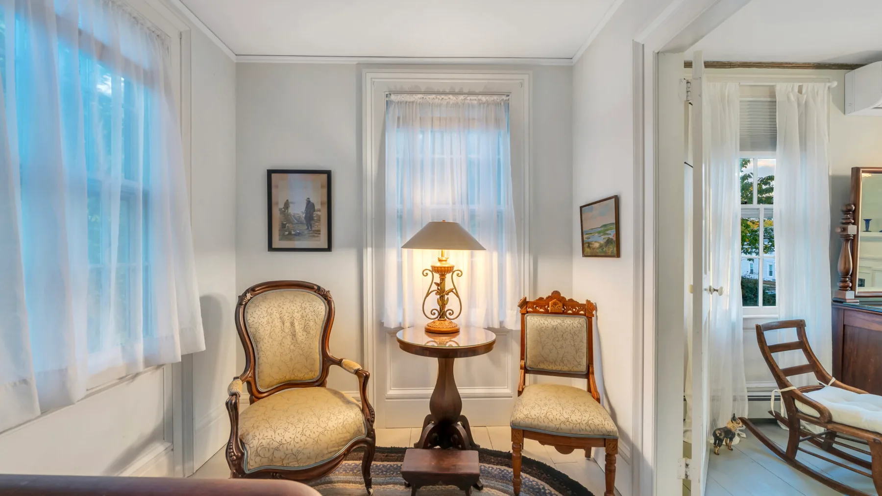Una sala luminosa con dos asientos tapizados y una mesa pequeña junto a la ventana.