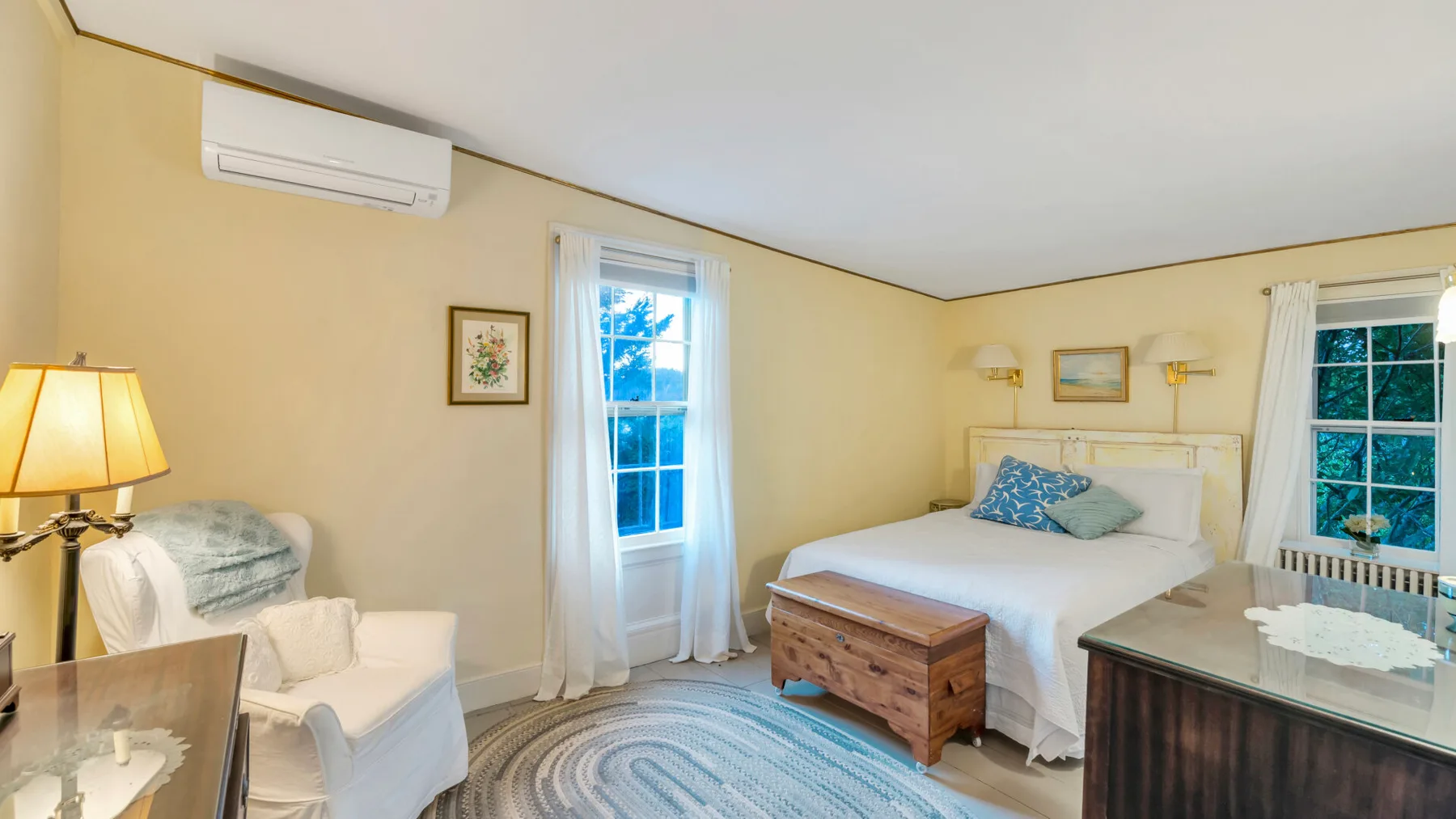 Un dormitorio con una cama, una zona de estar y una alfombra junto a las ventanas.