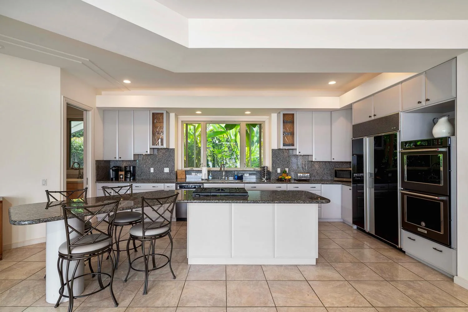 A bright kitchen with a central island, counter seating, and large windows.