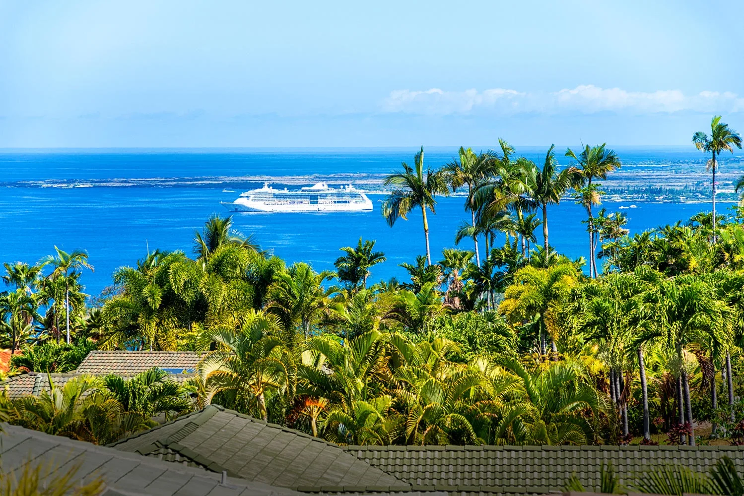A tropical ocean view stretches beyond dense greenery and palm trees.