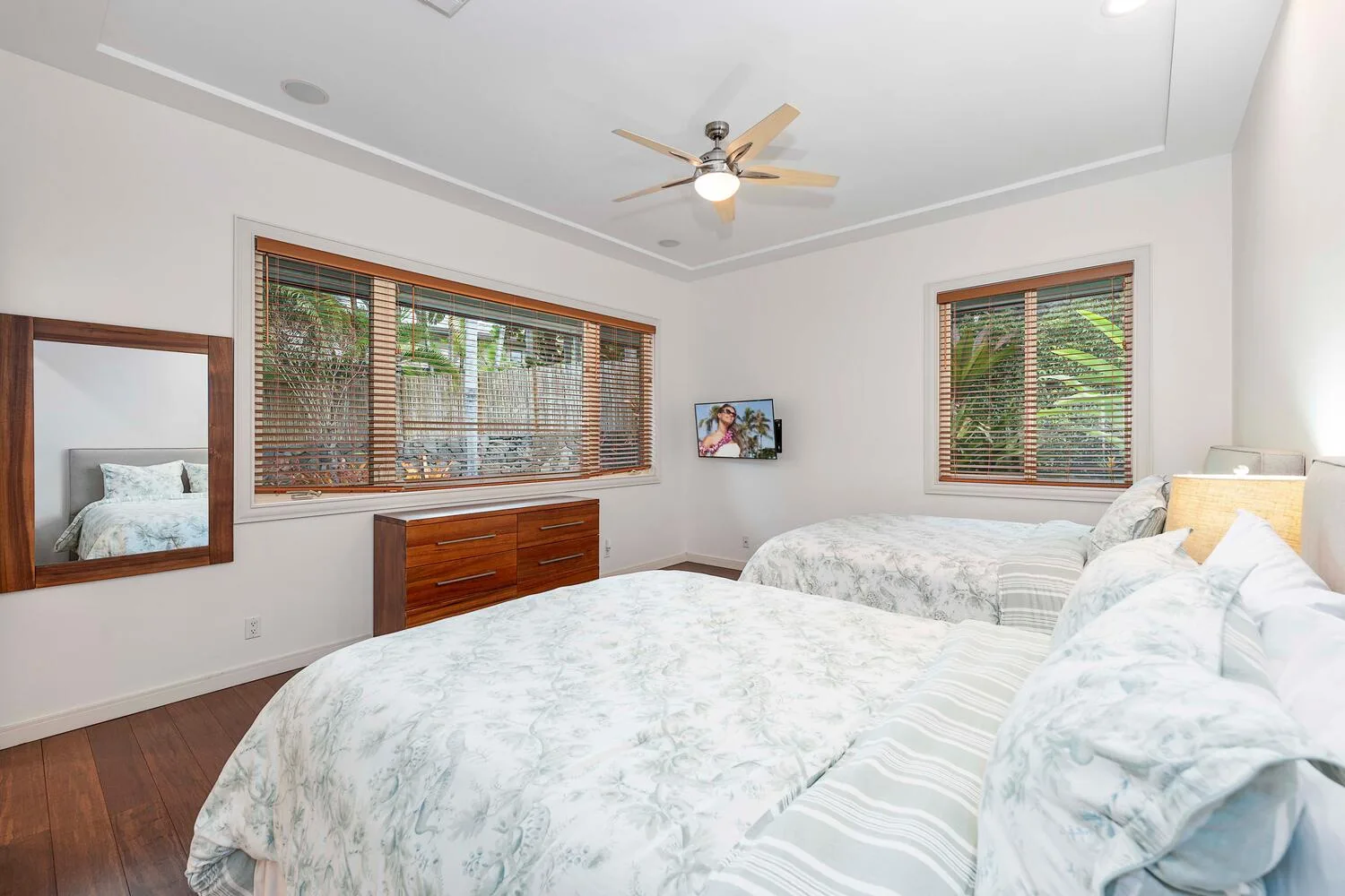 A bright bedroom with two beds and wooden blinds over the windows.