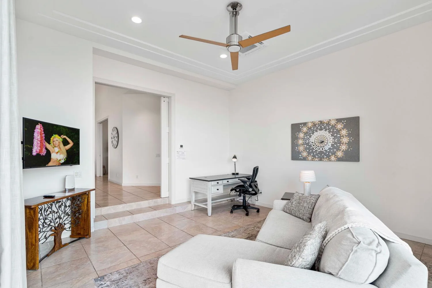 A bright living room with a white seating area and a desk near the doorway.