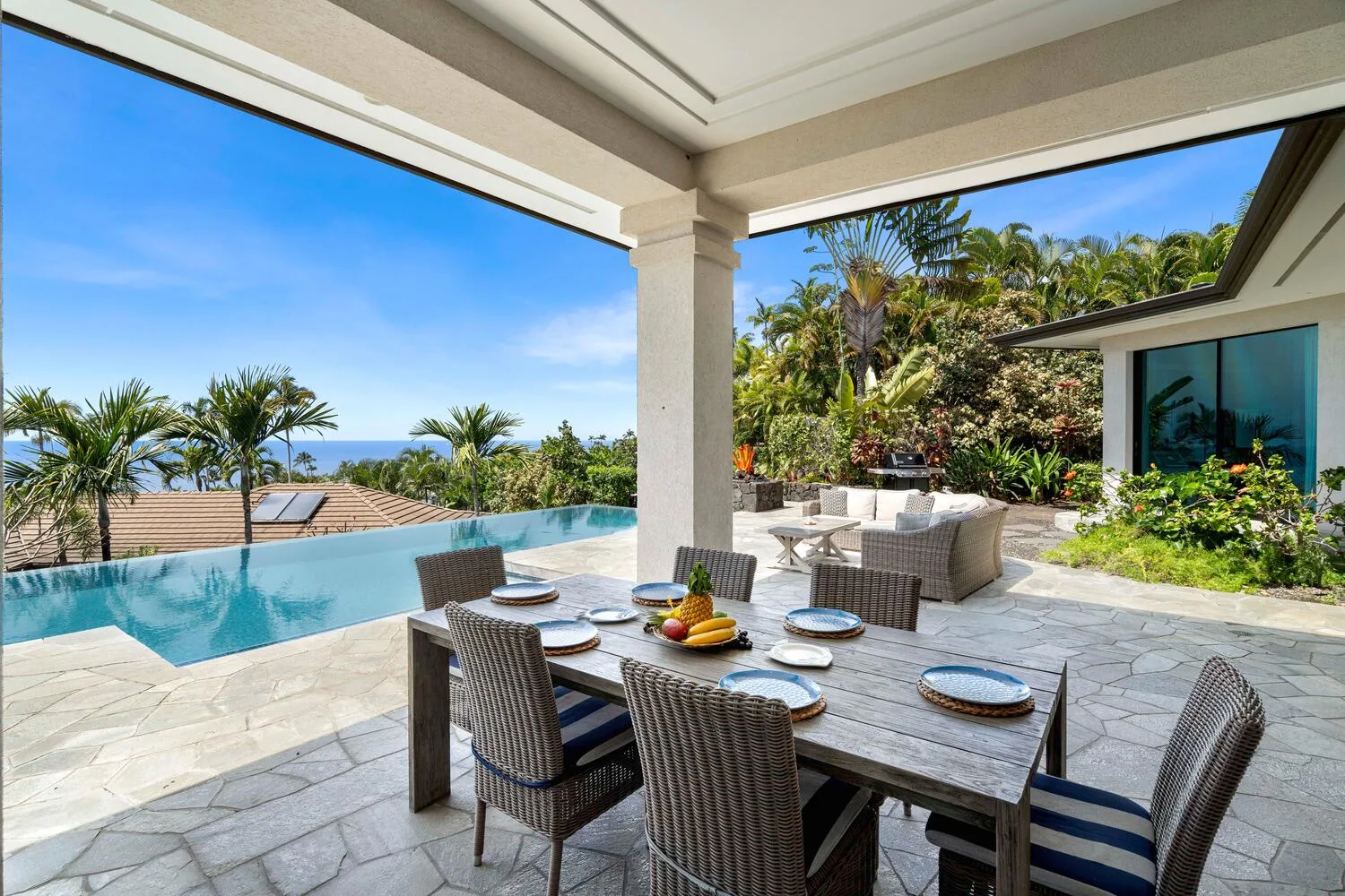 A covered patio dining area overlooks a swimming pool and tropical garden.