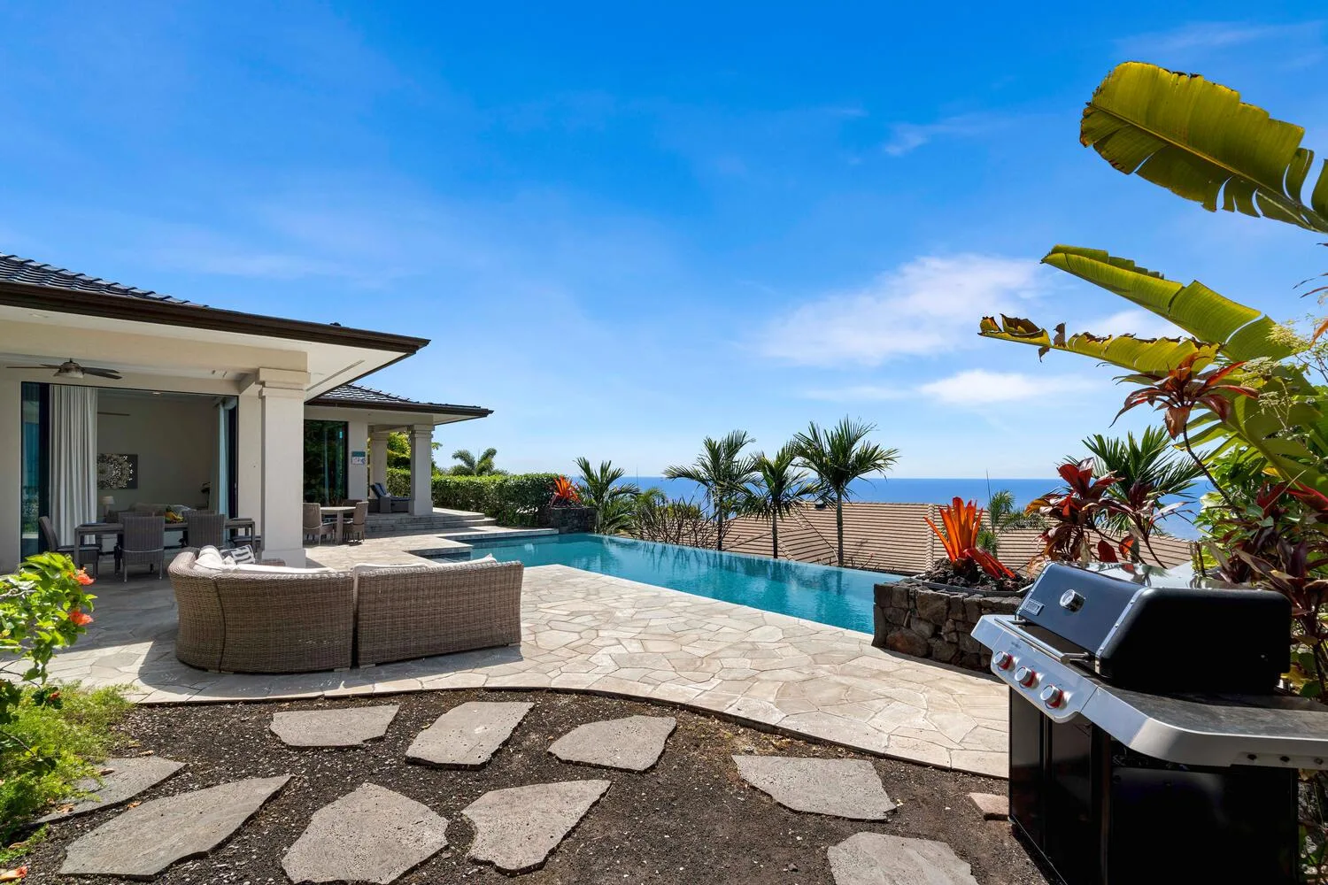 A patio and swimming pool overlook the ocean, with outdoor seating and a grill.