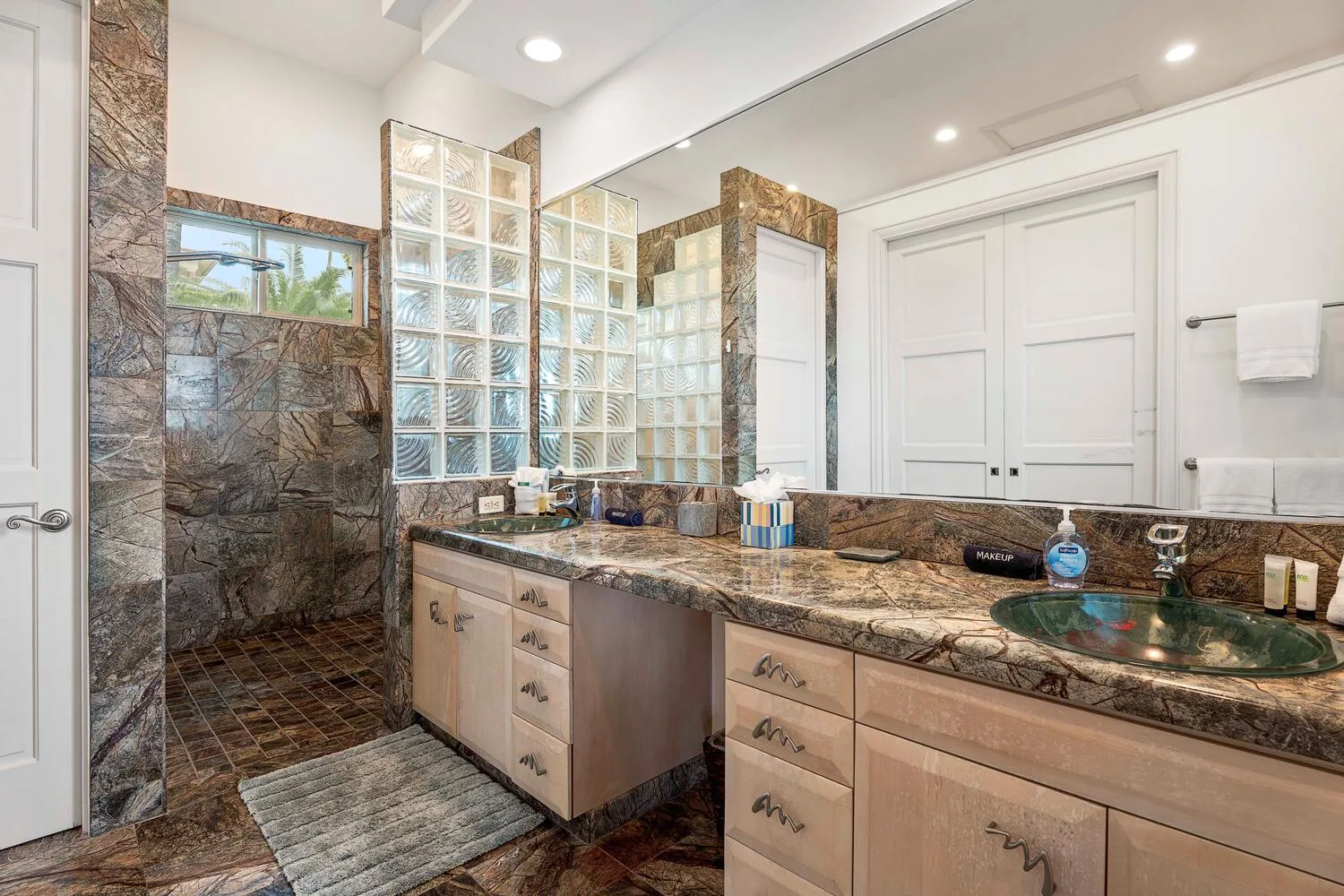 A bathroom with a glass-block shower area and a long vanity.