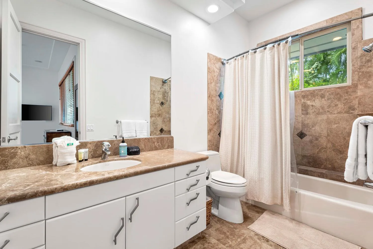 A bathroom with a long vanity, sink, toilet, and bathtub behind a curtain.