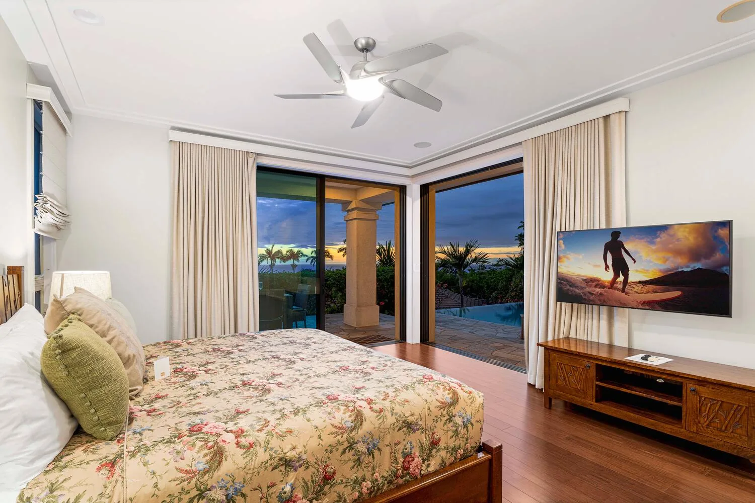 A bedroom with a floral bedspread, glass doors, and a television on the wall.