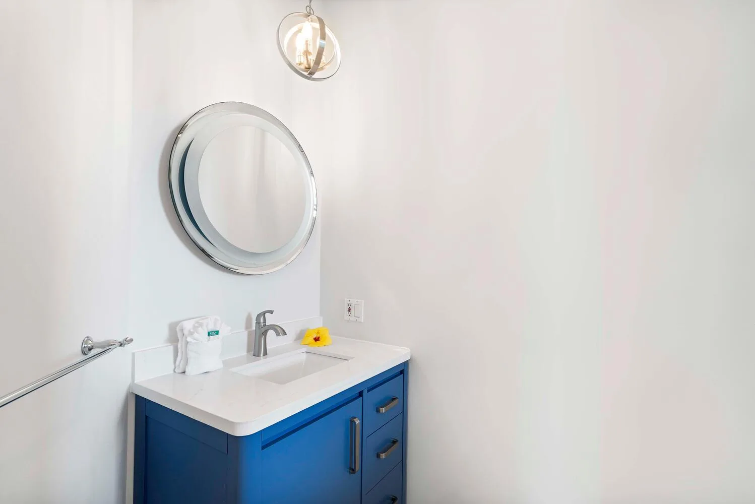 A bathroom vanity with a round mirror and blue cabinet.