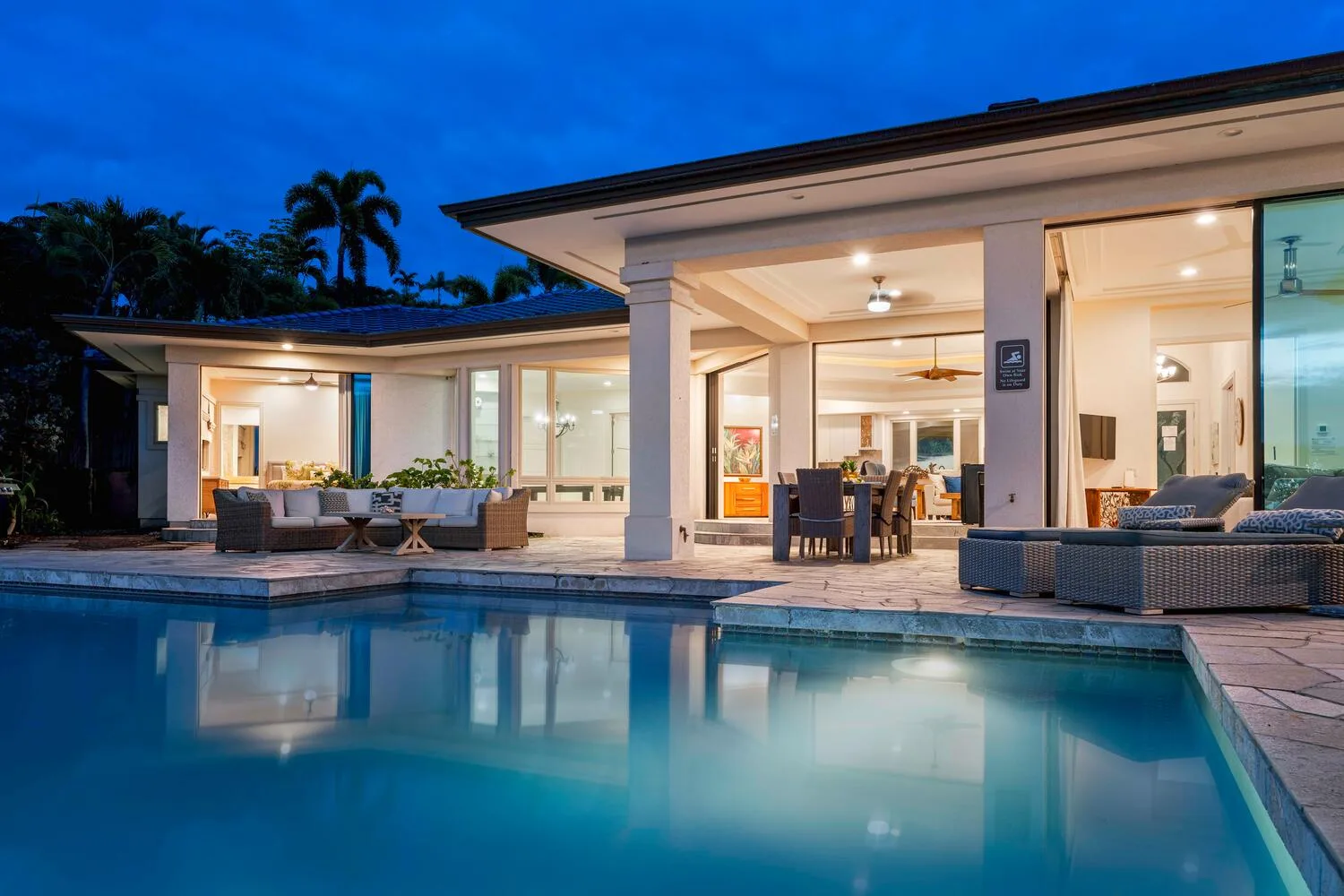 A modern house and outdoor seating are illuminated beside a swimming pool at dusk.