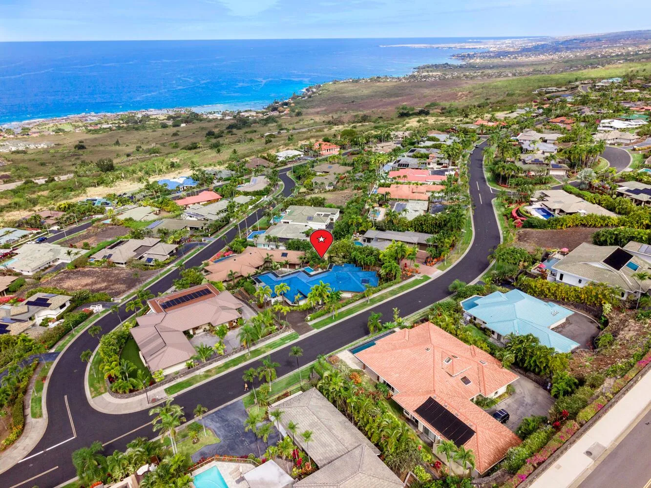 An aerial view shows a coastal neighborhood with winding roads and the ocean beyond.
