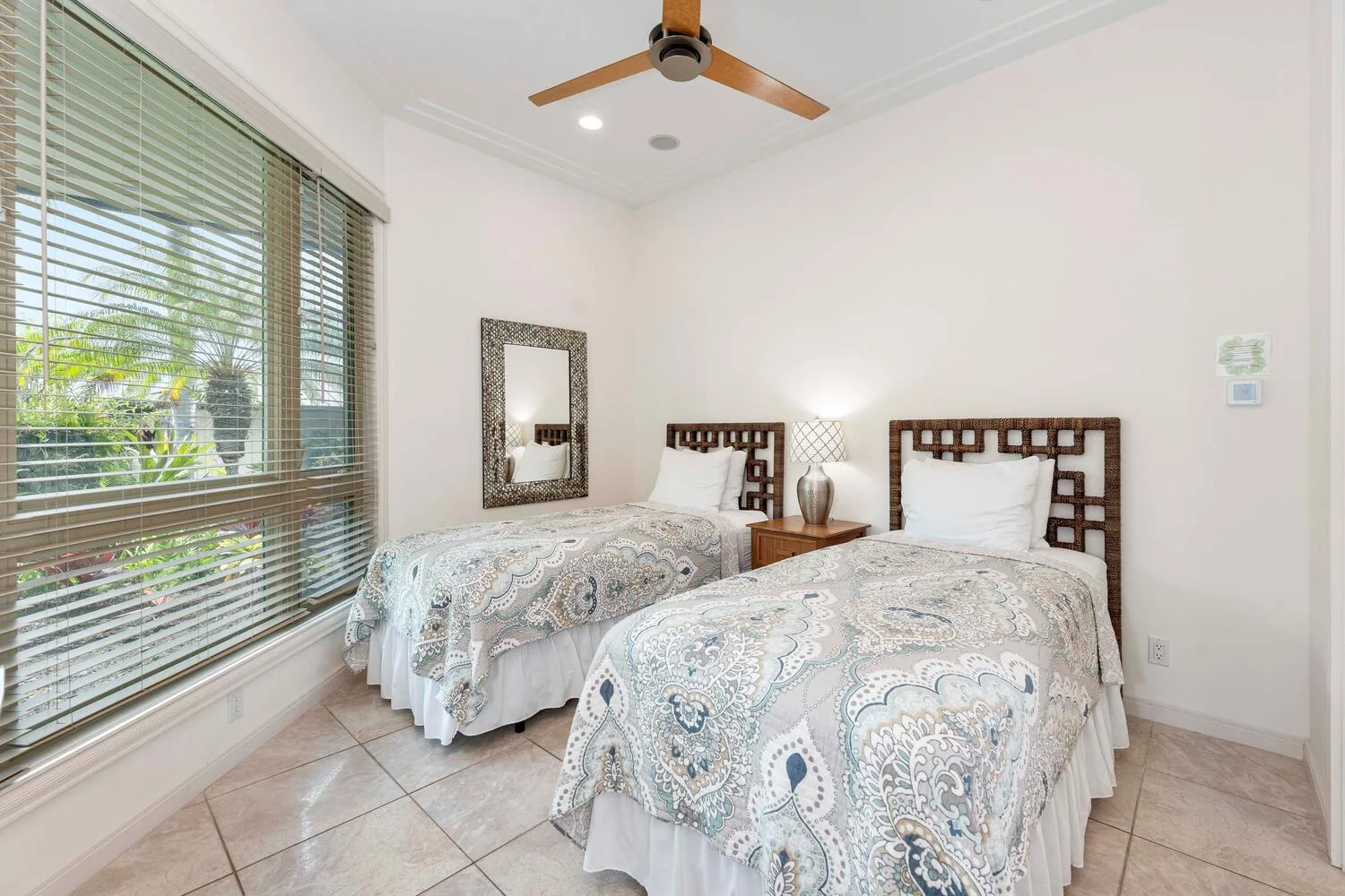 A bright bedroom with two beds and a large window with blinds.