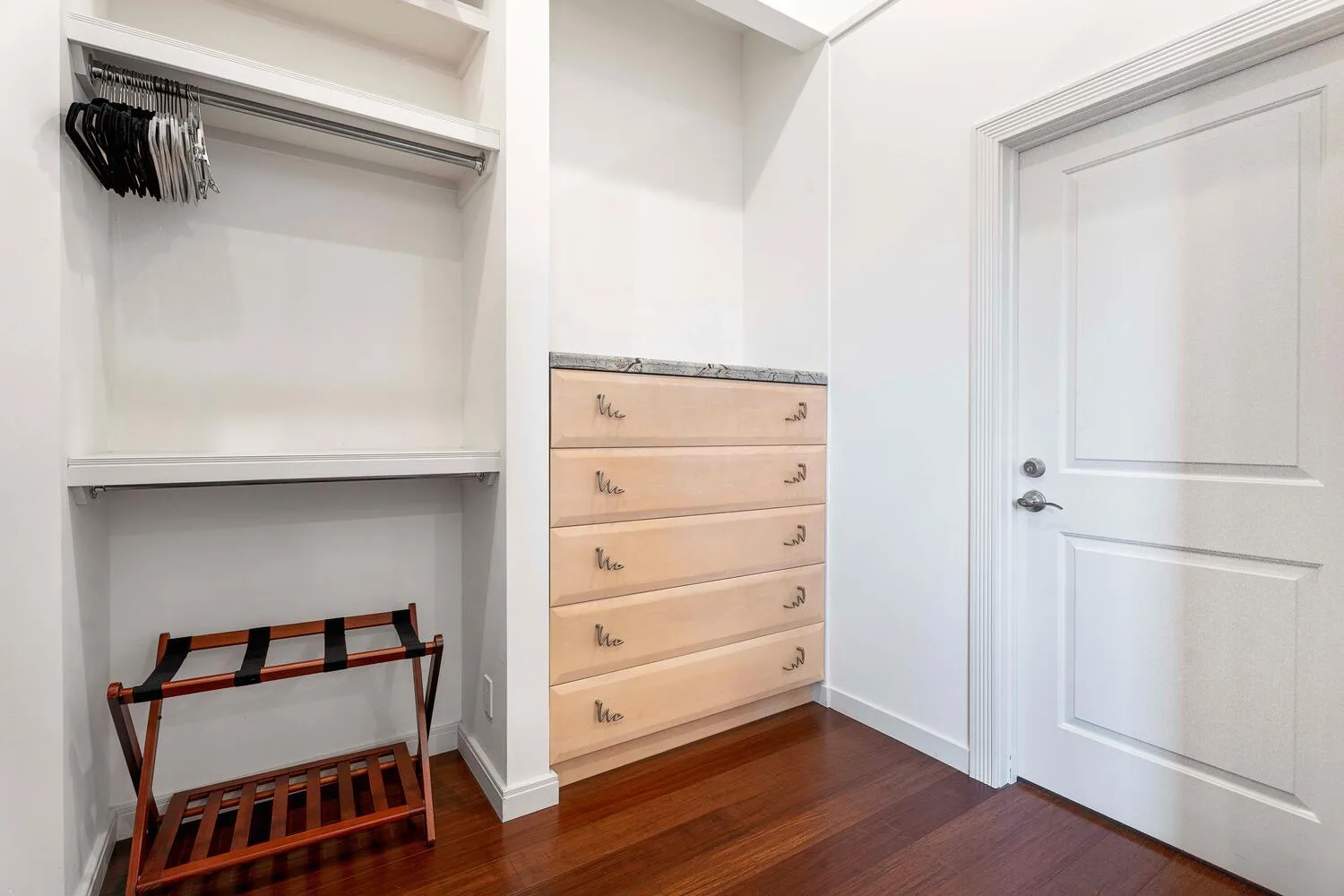 A bedroom closet area with open shelving, drawers, and a closed door.