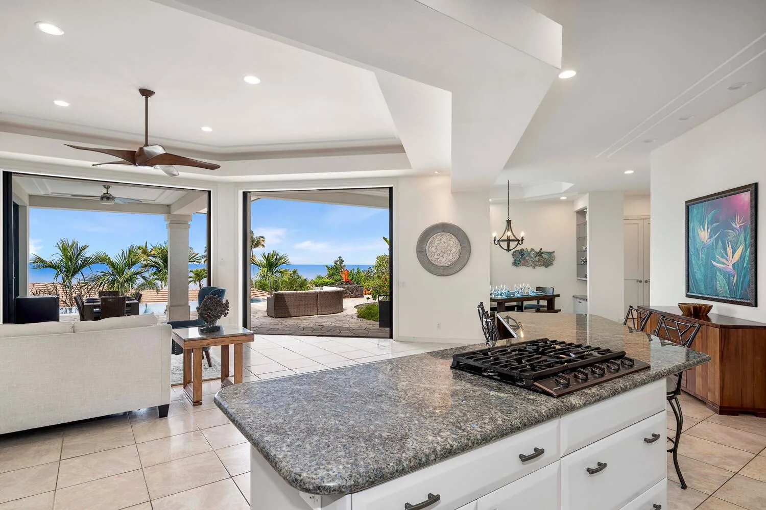 An open-plan kitchen and living area opens onto a patio with palm trees.