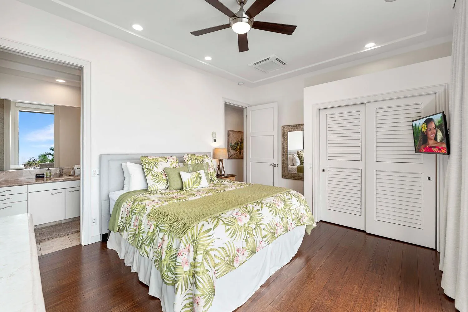 A bright bedroom with a bed dressed in green floral bedding and a ceiling fan.