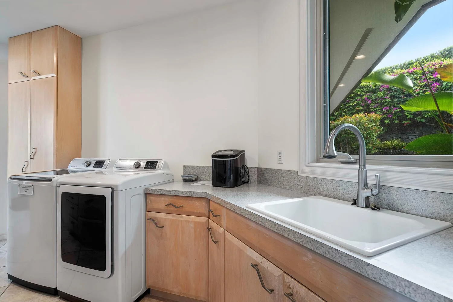 A laundry room with a washer, dryer, and a sink beneath a window.