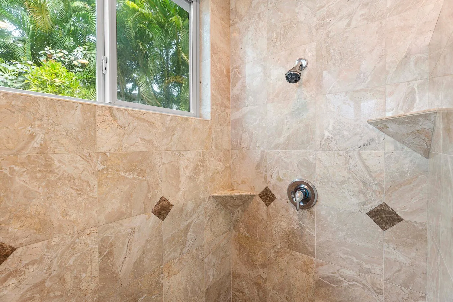 A tiled shower area with a window overlooking green foliage.
