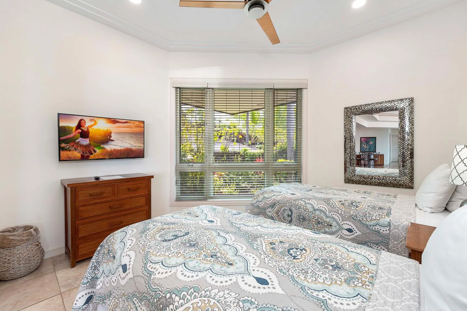 A bright bedroom with patterned bedding and a wide window with blinds.