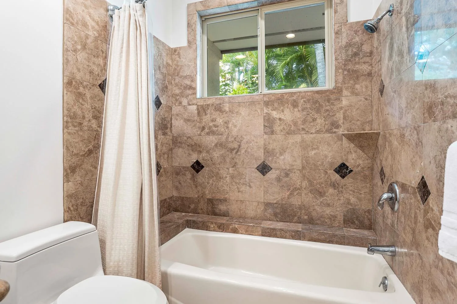 A tiled bathroom with a bathtub, shower curtain, and window.