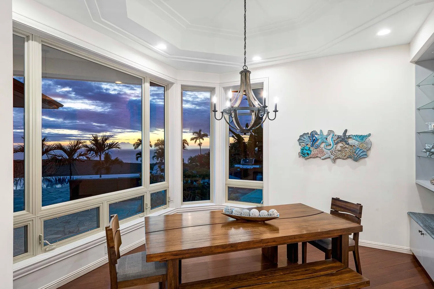 A dining area with a wooden table, decorative wall art, and large windows overlooking the water.